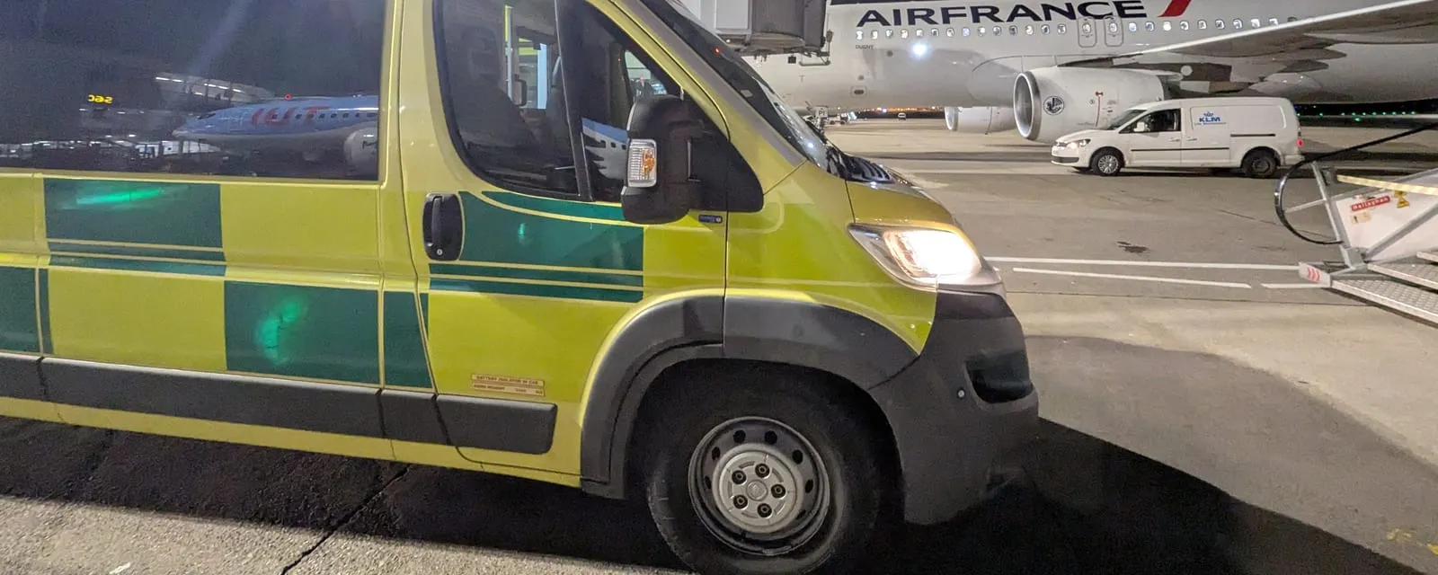 An ambulance waiting airside at night alongside a commercial airliner