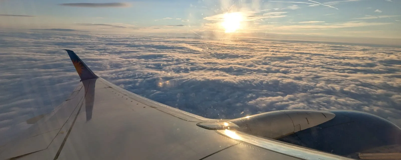 The wing of an airliner above an unbroken cloud layer at sunrise on a long-haul sector