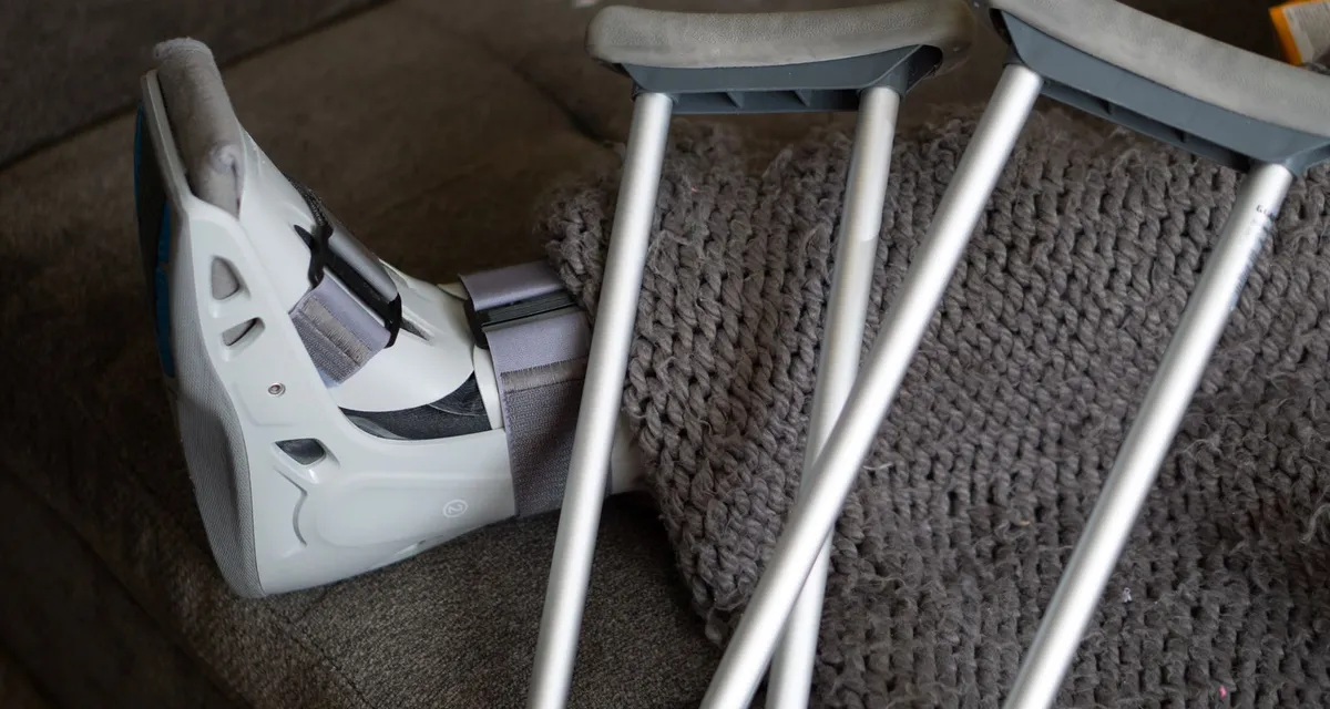 An orthopaedic walking boot resting on a sofa beside a pair of elbow crutches
