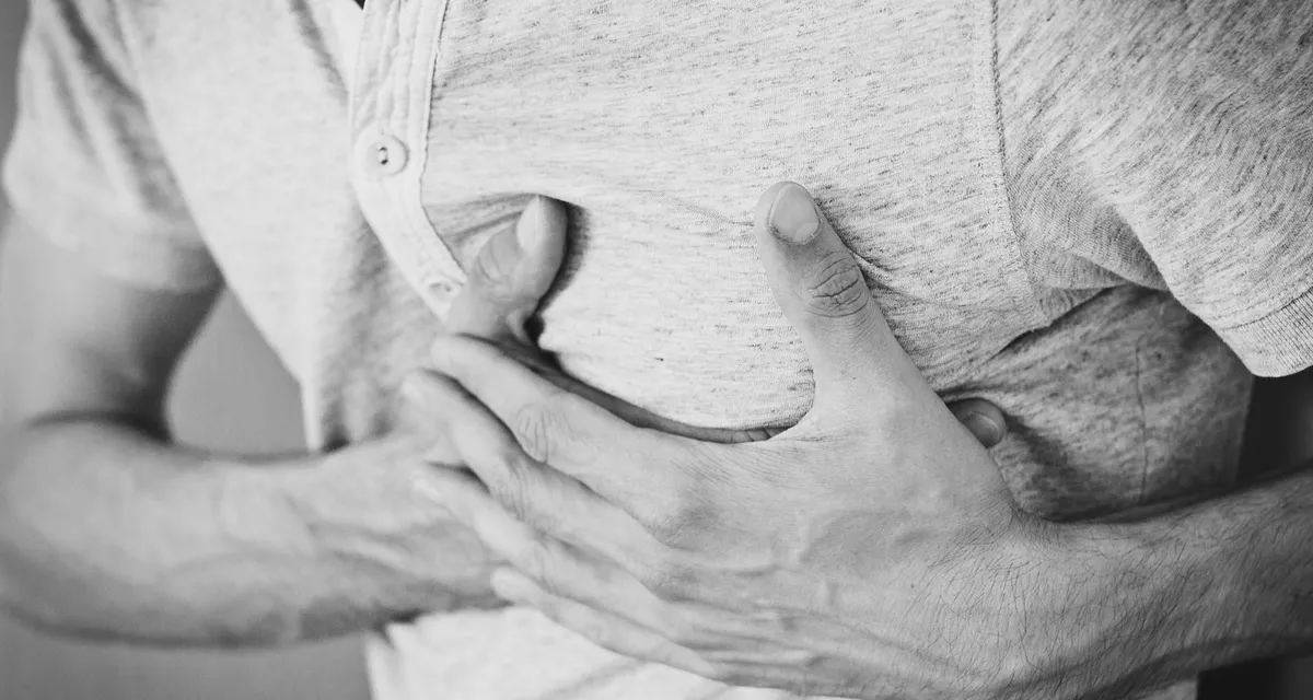 A black and white close-up of a man pressing a hand to his chest, face not shown