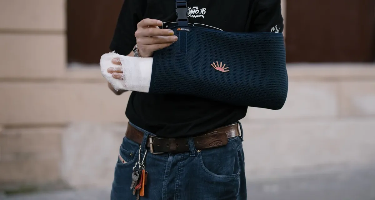 A man with his forearm and wrist bandaged, resting in a dark arm sling