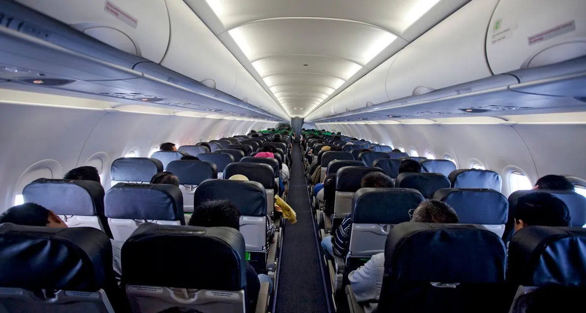The aisle of a full long-haul aircraft cabin, seen from behind the passengers