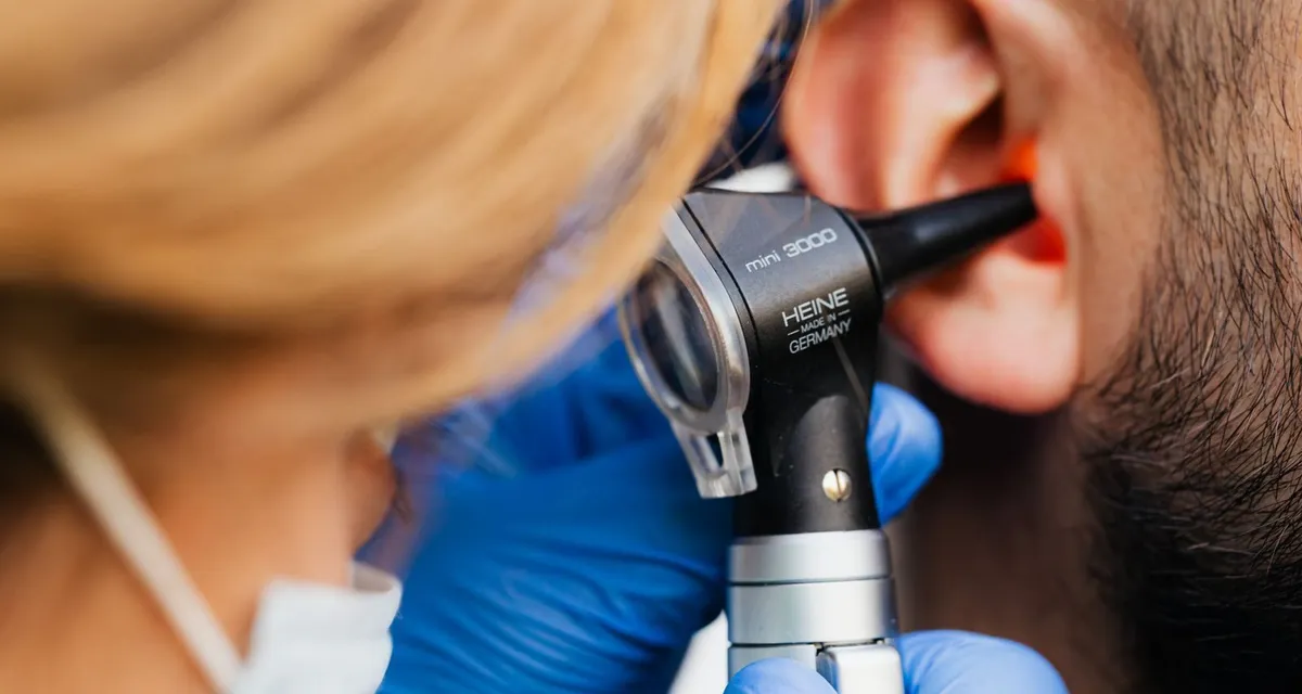A clinician in blue gloves examining a man’s ear with an otoscope