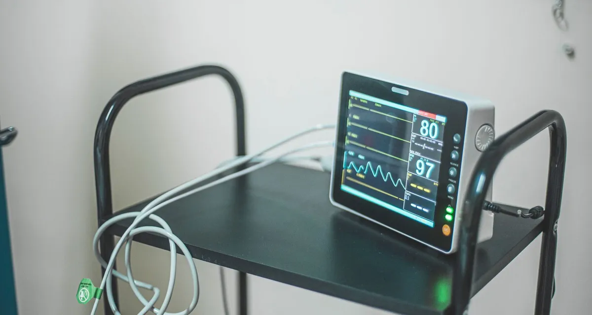 A bedside patient monitor on a trolley showing a heart rate trace