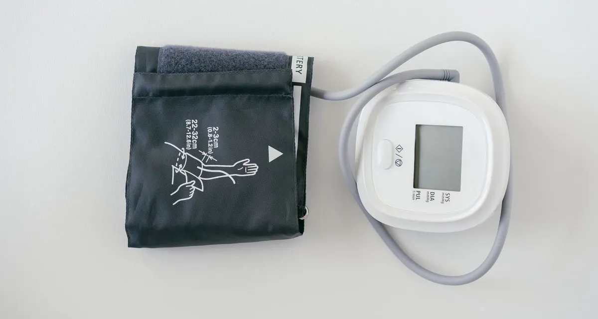 A blood pressure cuff and digital monitor laid out on a pale grey surface