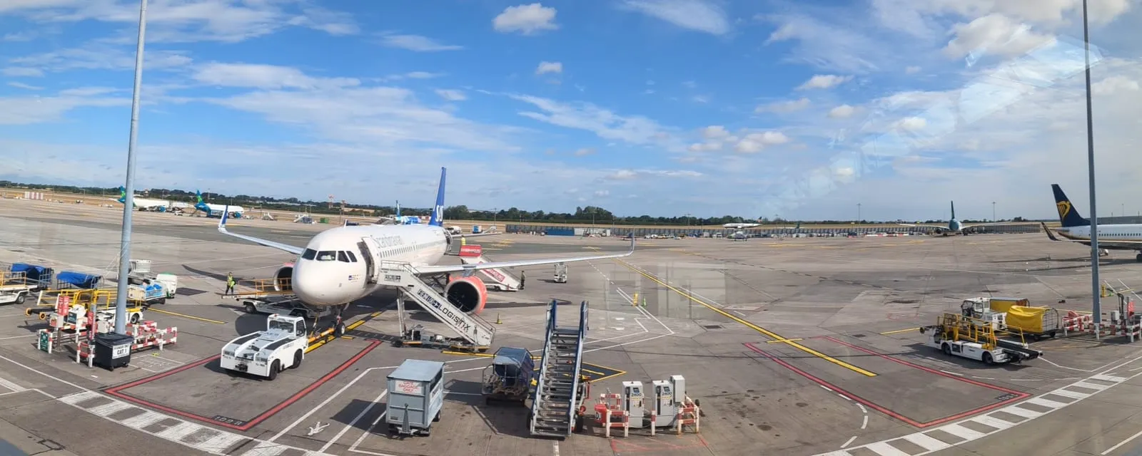 A wide apron view of an airport stand, with an aircraft on airstairs and ground handling equipment in position