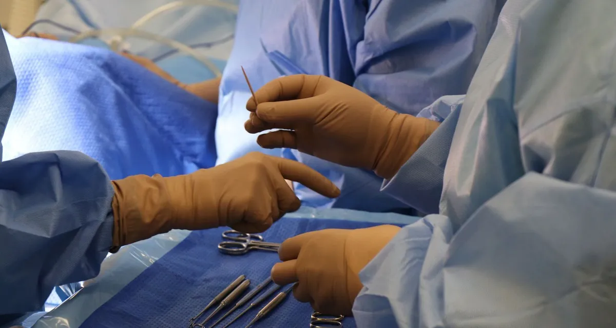Gloved hands passing surgical instruments across a sterile drape in an operating theatre
