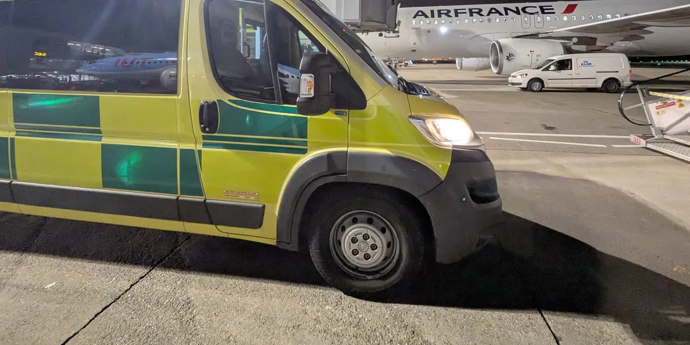 An ambulance waiting airside at night alongside a commercial airliner, ahead of a stretcher repatriation on a scheduled service