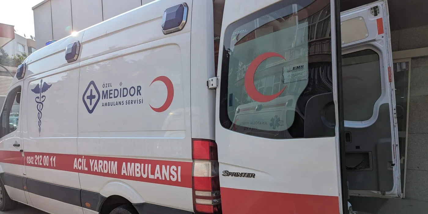 A partner ground ambulance with its rear doors open outside an overseas hospital at the start of a repatriation
